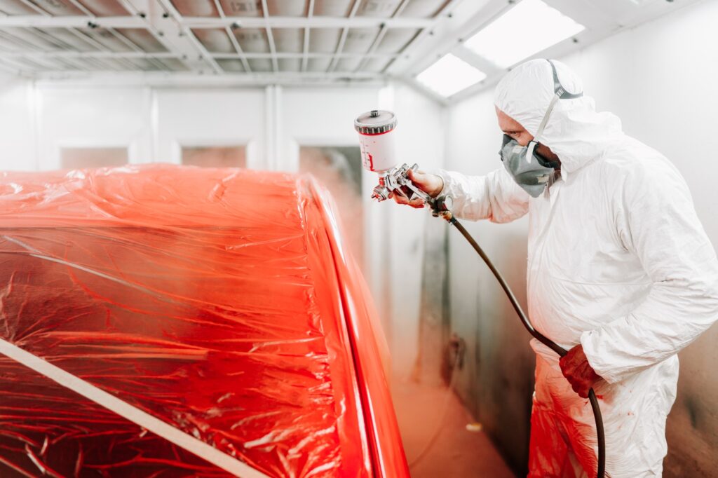 automotive industry engineer using spray gun and painting a red car